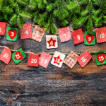 Christmas tree branches with Advent calendar on dark wooden background.