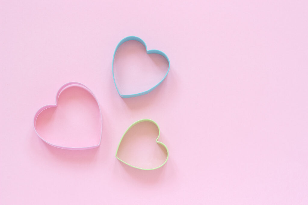 3 colorful cutters cookies in heart shape on pastel pink background.