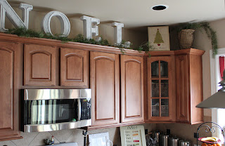 Brown kitchen cabinets with white letters that spell NOEL. Green garland 