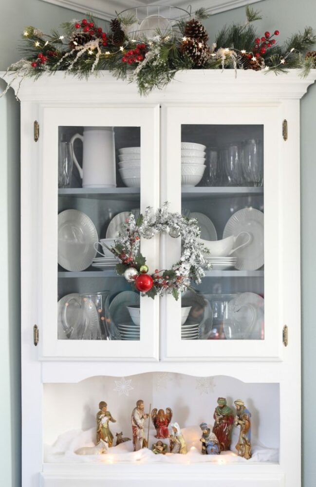 white cabinet with berries, pinecones and lights 