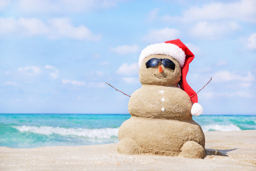 Snowman with Santa hat, made of sand on the beach. 