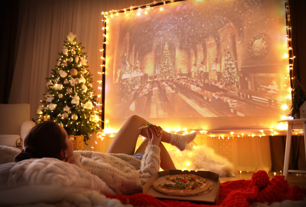 Female watching Harry Potter on large projection screen with Christmas lights and tree nearby.