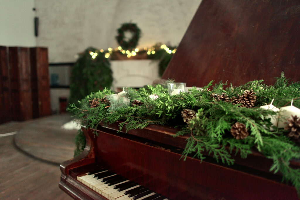 Green garland with pinecones, and white candles on a wooden piano 