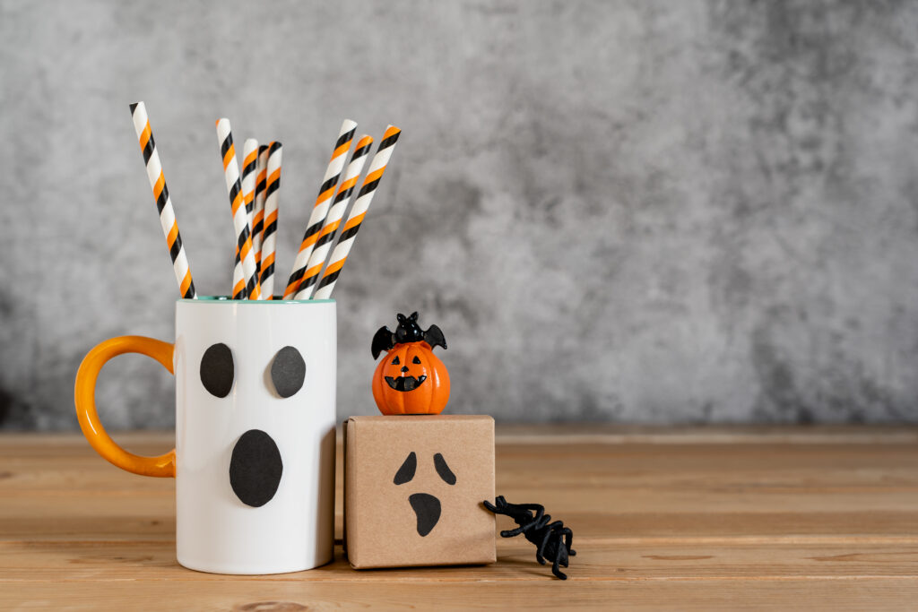 Ghost mug with Halloween pencils and gift boxes on a table. 