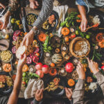 large table with lots of food and hands passing food