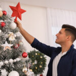 man placing red star on top of Christmas tre